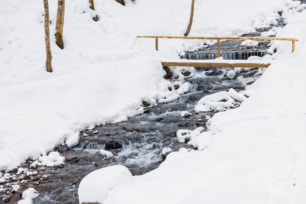 Pequeño puente de madera sobre un arroyo de montaña fría en un valle forestal de invierno