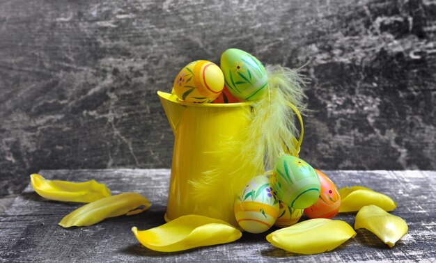 Pequeno regador amarelo com ovos de Páscoa em fundo de madeira