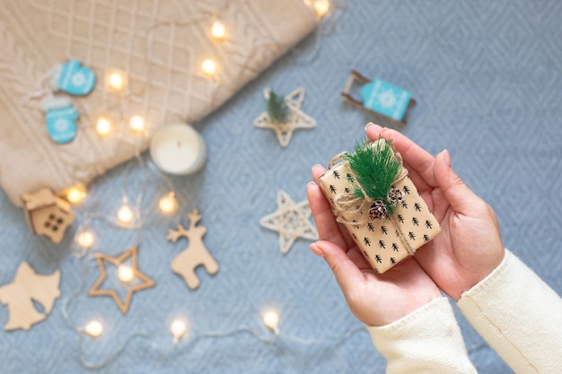 Un pequeño regalo de Navidad en las palmas de las mujeres sobre un fondo de una tela escocesa tejida azul