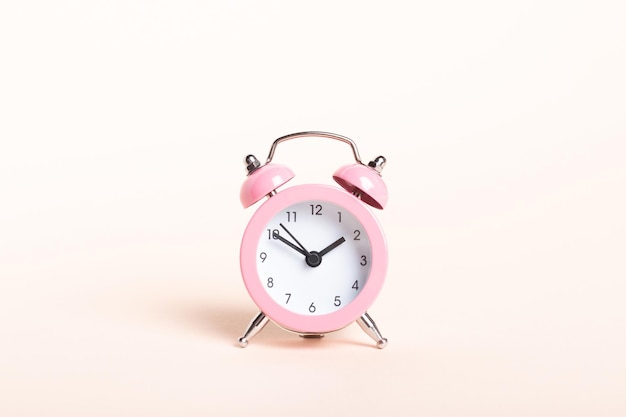 Pequeño reloj despertador rosa sobre un fondo rosa