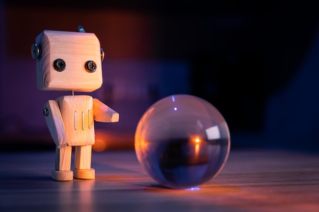 Un pequeño robot de juguete de madera mira una bola de vidrio en el fondo oscuro de papel tapiz azulado con poca luz