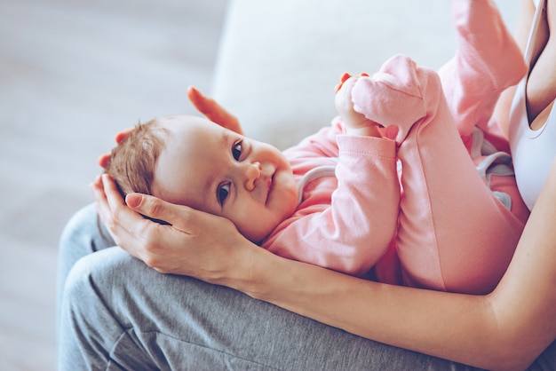 Pequeno tesouro. Feche a vista lateral de uma jovem segurando uma menina sorridente de joelhos enquanto está sentada no sofá