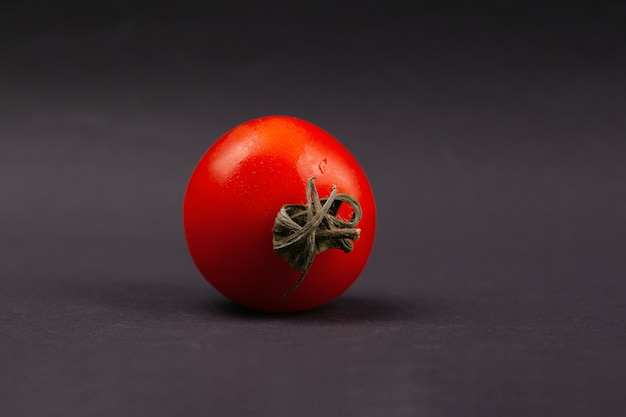 Foto pequeño tomate de cereza fresco brillante en un primer negro del fondo. vegetal.