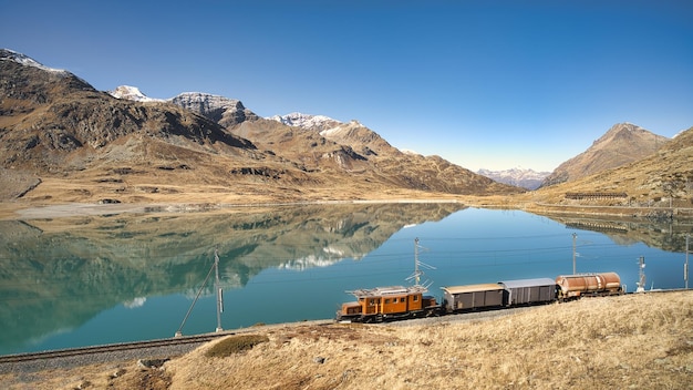 Pequeño tren de carga sobre raíles cerca de un lago de alta montaña