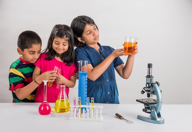 Pequenos alunos indianos curiosos ou cientistas estudando ciências, fazendo experiências com produtos químicos ou microscópio em laboratório, foco seletivo