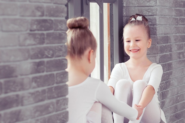 Pequeños amigos niños bailando ballet sentados en el alféizar de la ventana y abrazándose mientras sonríen juntos
