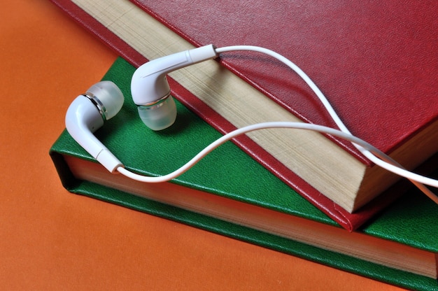 Pequeños auriculares blancos con cable se encuentran encima de una pila de libros. de cerca