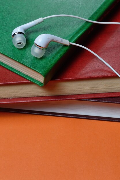 pequeños auriculares blancos con cable se encuentran encima de una pila de libros. de cerca