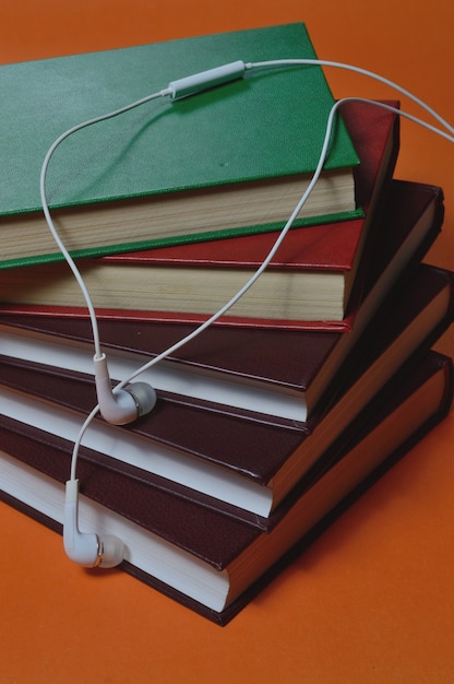 pequeños auriculares blancos con cable se encuentran encima de una pila de libros. de cerca