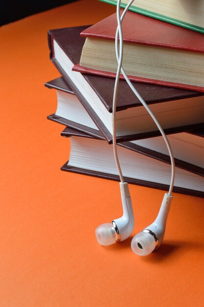 Pequeños auriculares blancos del teléfono yacen sobre una pila de libros.