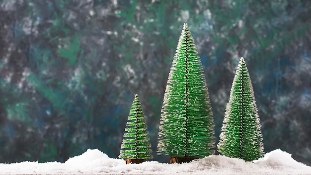 Pequenos brinquedos de árvore de Natal em neve no inverno Conceito de Ano Novo Composição festiva em fundo azul com luzes e flocos de neve