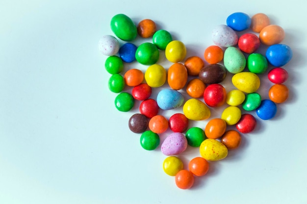 Pequeños caramelos multicolores en forma de corazón sobre un fondo blanco con espacio para escribir texto