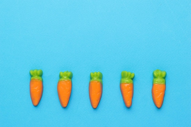 Pequeños dulces en forma de zanahorias sobre un fondo azul Concepto de cosecha mínima Foto creativa