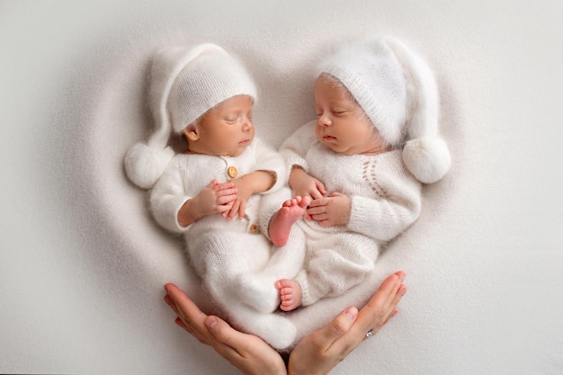 Pequeños gemelos recién nacidos con monos blancos sobre un fondo blanco Los gemelos recién nacidos duermen junto a su hermano en el fondo del corazón La madre de los padres sostiene a los niños con las manos con las palmas