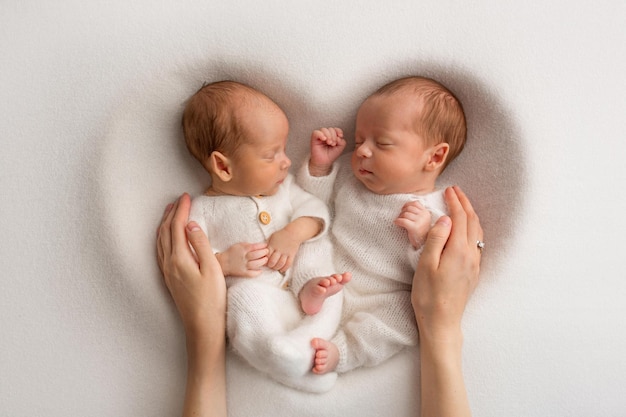 Pequeños gemelos recién nacidos con monos blancos sobre un fondo blanco Los gemelos recién nacidos duermen junto a su hermano en el fondo del corazón La madre de los padres sostiene a los niños con las manos con las palmas