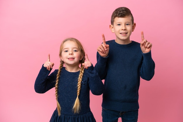 Pequeños hermanos caucásicos aislados de fondo rosa apuntando a una gran idea