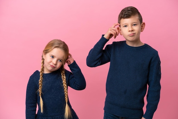 Pequenos irmãos caucasianos isolados em fundo rosa com dúvidas e com expressão de rosto confuso