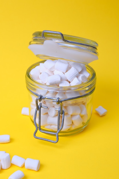 Pequenos marshmallows brancos em uma jarra em um espaço de cópia de fundo amarelo