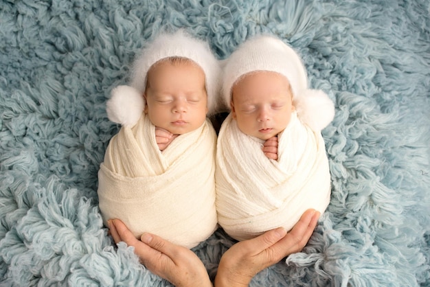 Pequenos meninos gêmeos recém-nascidos em casulos brancos em um fundo azul em bonés brancos Fotografia profissional de estúdio de gêmeos recém-nascidos Foto de alta qualidade