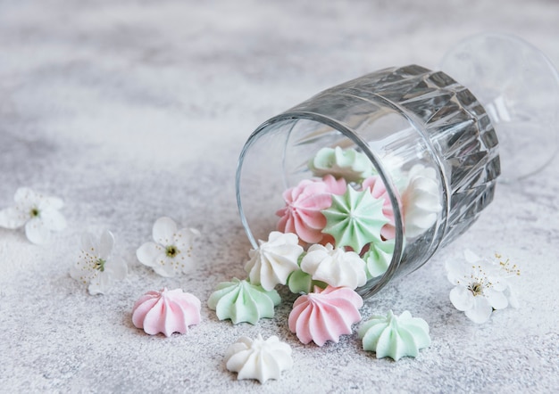 Pequeños merengues blancos rosados y verdes en el vaso sobre superficie de hormigón