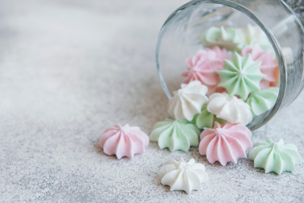 Pequeños merengues blancos rosados y verdes en el vaso sobre superficie de hormigón