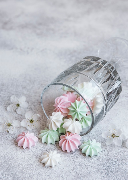 Pequeños merengues blancos rosados y verdes en el vaso sobre superficie de hormigón