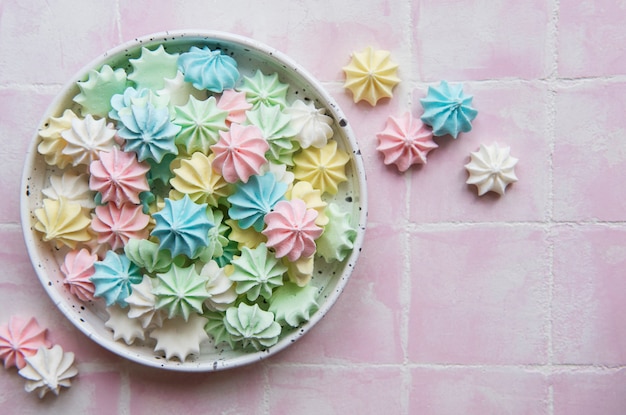 Pequeños merengues de colores en el cuenco de cerámica sobre fondo de mosaico rosa