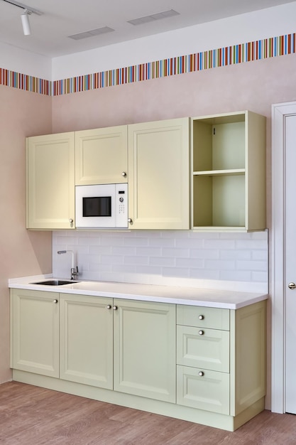 Pequeños muebles de cocina de estilo decorativo clásico con fregadero y horno microondas cerca de la puerta blanca