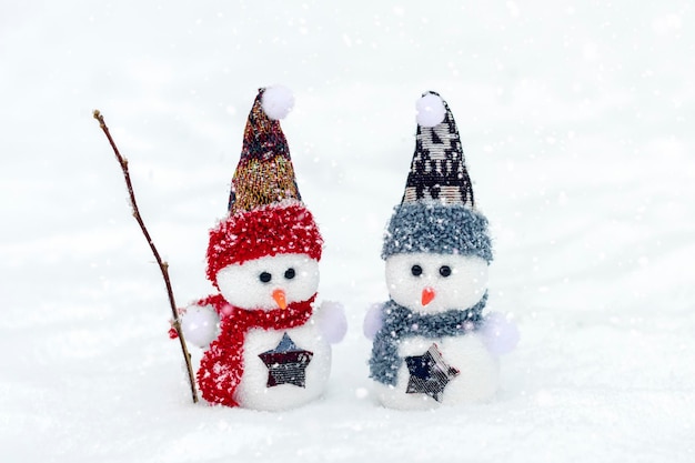 Pequeños muñecos de nieve felices con gorra azul roja y bufanda de pie en el fondo de la nieve invernal