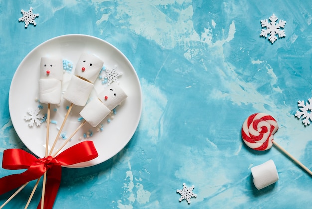 Pequeños muñecos de nieve de malvaviscos en palos. piruletas y copos de nieve. comida navideña.