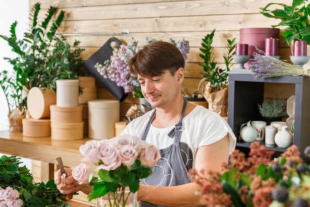 Pequenos negócios. Florista masculina fazendo buquê de rosa na loja de flores. Assistente ou proprietário em um estúdio de design floral, fazendo decorações e arranjos. Entrega de flores, criação de pedido