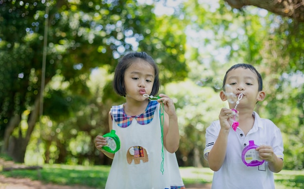 Pequeños niños asiáticos soplando burbujas, jugando con alegría y felicidad en la hermosa y verde naturaleza.
