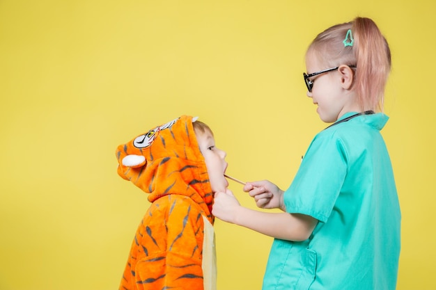 Pequeños niños caucásicos juegan al médico, el niño disfrazado de tigre muestra la garganta al pediatra en la cita con el médico