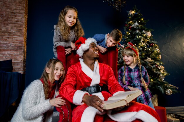 Pequeños niños hermosos escuchan la historia que lee Santa Claus