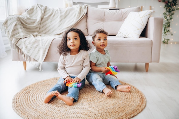 Pequeños niños negros afroamericanos jugando con juguetes pop en el suelo en casa