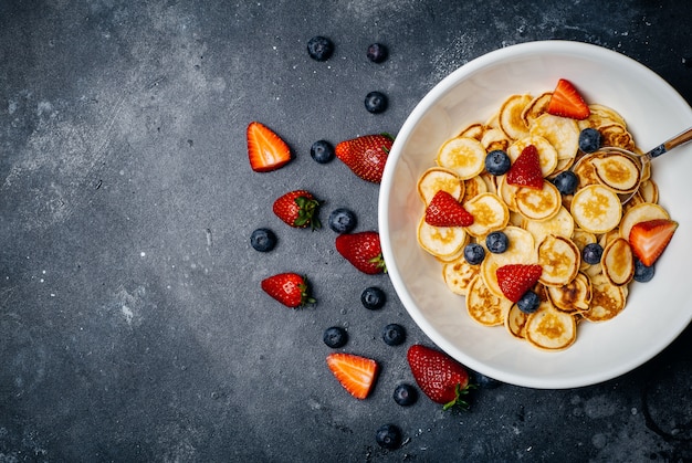 Pequeños panqueques para el desayuno. Panqueques con fresas y arándanos cocinados en la mañana para el desayuno en la cocina de casa.