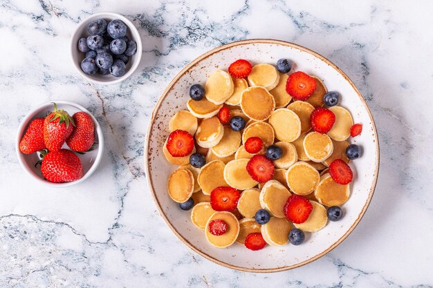 Pequeños panqueques con fresas y arándanos para el desayuno. Vista superior.