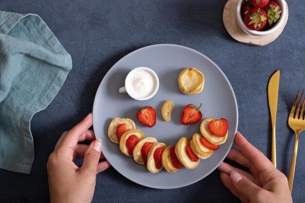 Pequeños panqueques con fresas en la porción original en forma de cara sonriente Vista superior Lay Flat