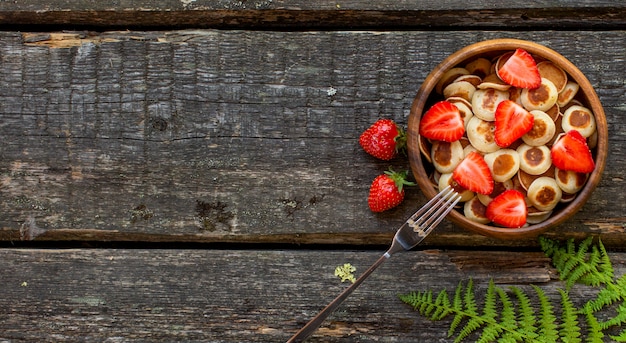 Pequeños panqueques de panqueques de cereales en un tazón de madera con fresas sobre un fondo de madera. Vista superior. Copia espacio