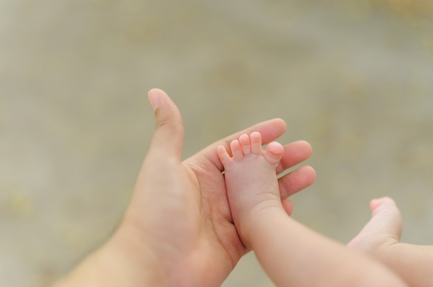 Foto pequeños pies de bebé en manos de las madres al aire libre. manos de madre