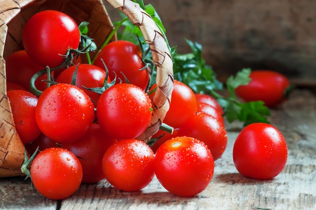 Pequeños tomates cherry rojos se derraman de una cesta de mimbre sobre una mesa de madera antigua con un enfoque selectivo de estilo rústico