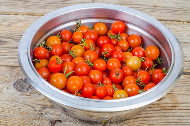 Pequeños tomates cherry rojos maduros en recipiente de metal sobre mesa de madera.