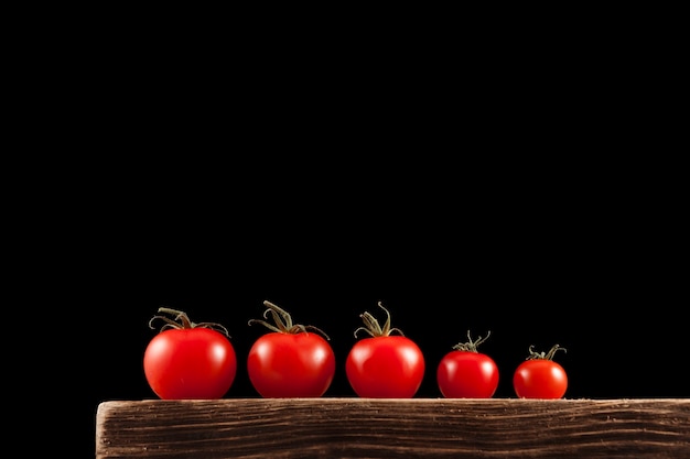 Pequeños tomates cherry rojos sobre una vieja tabla de madera marrón