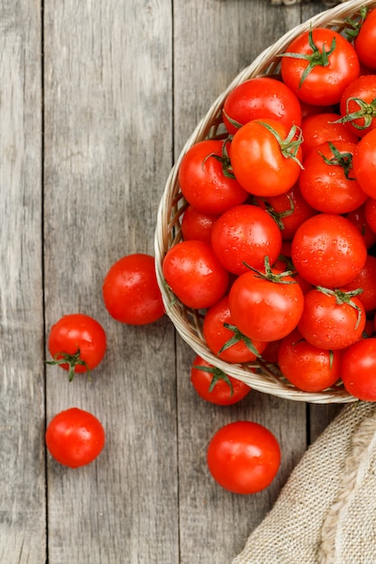 Pequeños tomates rojos en una cesta de mimbre en una vieja mesa de madera. Cereza madura y jugosa