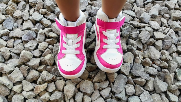 Peques pies de niña con zapatos rosados y blancos en las piedras