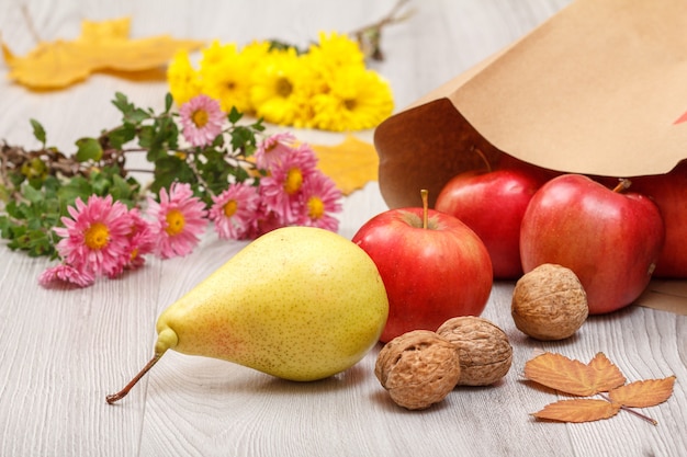 Pêra amarela madura, nozes, maçãs vermelhas com saco de papel e flores na mesa de madeira. Alimentos orgânicos saudáveis. Tema de outono.