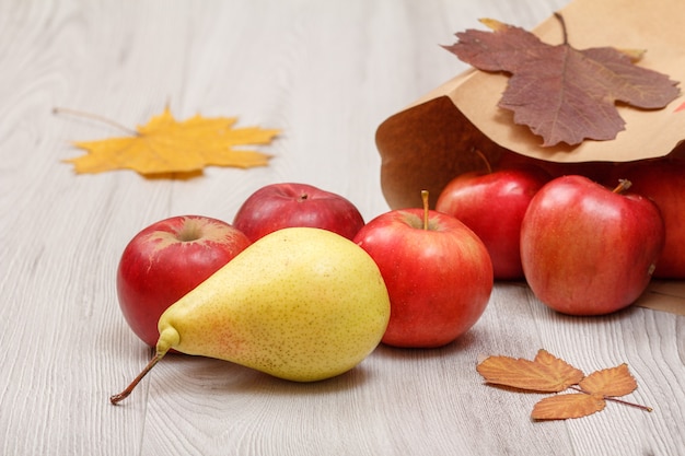 Pera amarilla madura, manzanas rojas con bolsa de papel y hojas secas en el escritorio de madera.