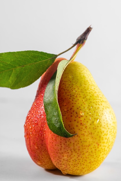 Pera madura fresca con gotas de agua y hojas sobre fondo blanco. Fruta sabrosa. Orientación vertical