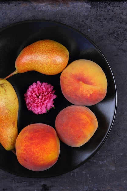 Peras e pêssegos em uma placa preta grupo de frutas coloridas de verão saudáveis em um fundo escuro closeup vista de cima