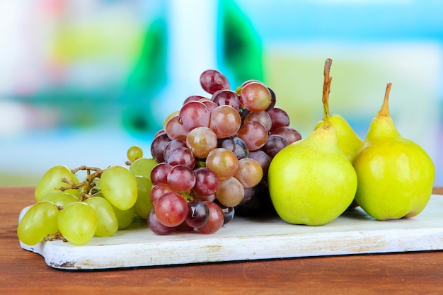 Foto peras e uvas na tábua de madeira sobre fundo brilhante